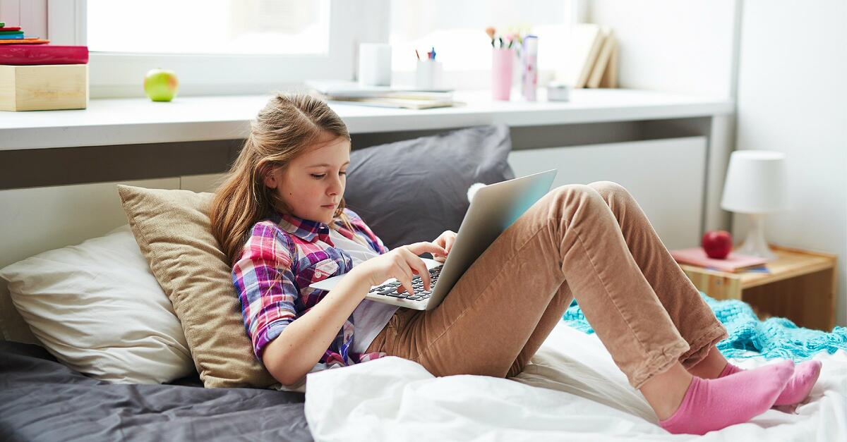 A young student lounges on top of her bed with her laptop